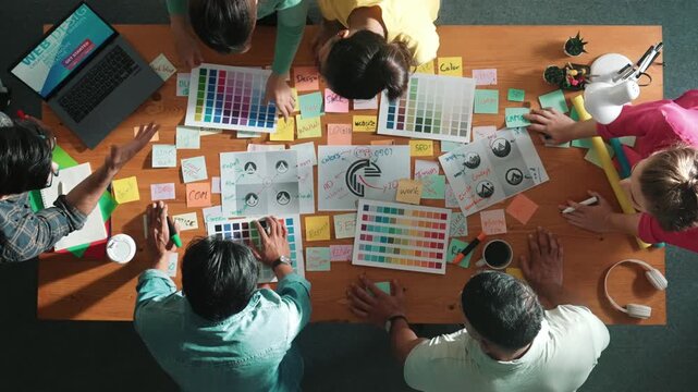 Top down view of designer compare color palettes with laptop and design product. Aerial view of marketing team working together to choose color while discussing about logo graphic design. Symposium.