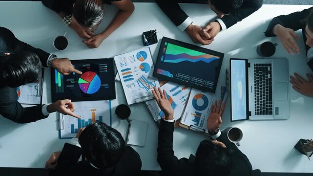 Top down aerial view of professional businessman handed out financial statistic to analyst data investment graph. Group of diverse investors brainstorming and planning marketing strategy. Directorate.
