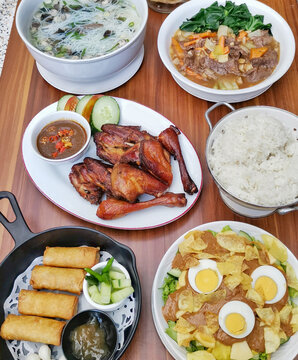Authentic Indonesian family-style dining featuring grilled chicken, spring rolls, vegetable dishes, rice, soup, peanut salad and sambal served on a rustic wooden table.