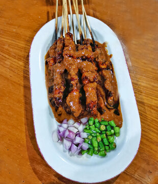 Close up of Indonesian chicken satay skewers with rich peanut sauce served on plate with chopped shallots and green chili. Authentic Asian street food dish.