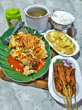 Authentic Indonesian family-style meal featuring crispy sweet and sour fish, chicken satay, gado-gado, steamed rice, clear vegetable soup and traditional side dishes.