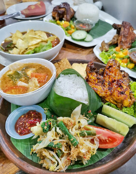 Authentic Indonesian grilled chicken rice set featuring ayam bakar, banana leaf rice, sambal, mixed vegetables, soup, tempeh and fresh cucumber served in a rustic restaurant.
