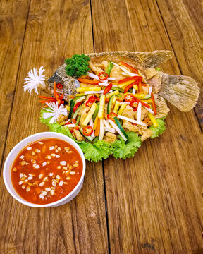 Authentic Indonesian gurame asam manis featuring whole crispy fried gourami topped with colorful vegetables and served with sweet and sour sauce on a rustic wooden table.