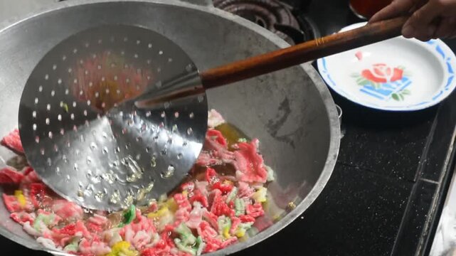 Close-up of frying colorful Indonesian crackers in hot oil. Traditional snack preparation featuring vibrant crackers, authentic local cuisine, homemade cooking, crispy texture, and delicious street fo