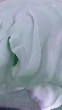 Vertical top down view of stirring cream in a circular motion using a metal spoon. Smooth mixing texture, beauty product preparation concept.