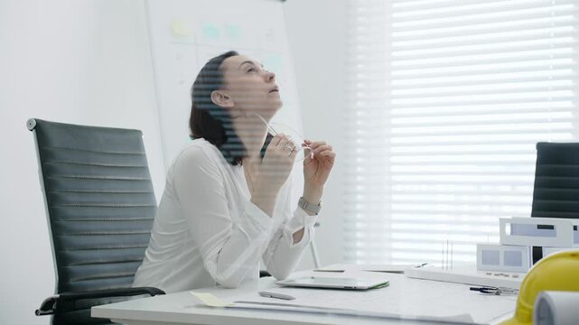 Female architect analyzing blueprints and architectural models in office, using digital tablet for modern design planning and engineering project development