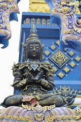 Obraz premium Seated meditating deity statue with folded hands against ornate temple wall