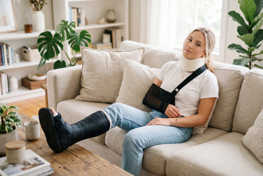 Injured woman with neck brace arm sling and leg cast on sofa