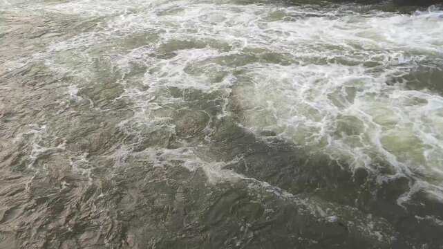 Rushing water flowing rapidly from a dam watergate under a bridge
