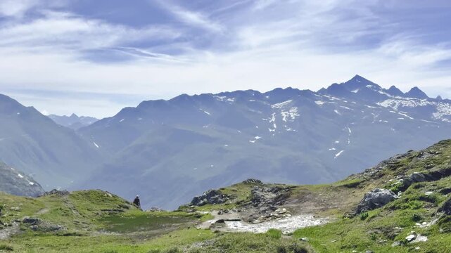 Lone hiker walking a meadow trail high above a deep valley facing