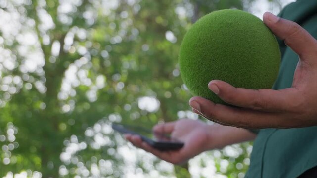 Business professional holding a green moss ball while using smartphone in natural outdoor environment, symbolizing sustainable business, ESG strategy, green innovation, environmental responsibility