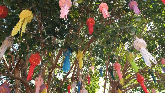 Clusters of vibrant handmade Lanna paper lanterns in red, yellow and green hanging from temple structures in northern Thailand