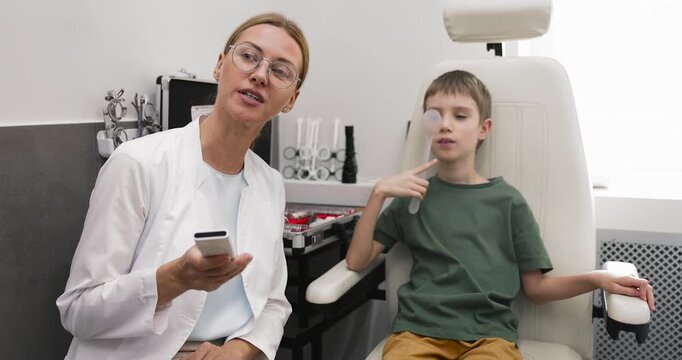 Female medical professional conducting visual acuity test on pediatric eye care appointment with little patient asking child to read letters using digital vision chart in modern ophthalmology clinic