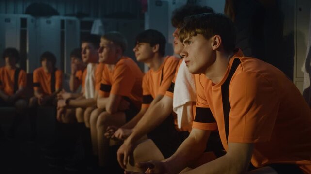 Close Up of Young Football Player in Orange Jersey in Locker Room. Boy Listens With Intense Concentration to Coach Post Training Briefing. Concentration, Tactical Understanding, and Dedicated Mindset.
