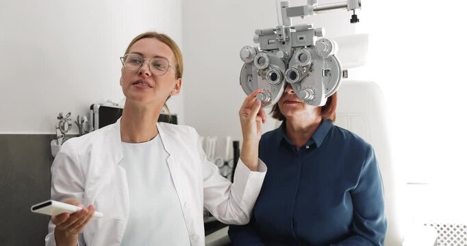 Professional ophthalmologist testing eyesight of middle aged woman patient in medical clinic using phoropter adjusting modern apparatus asking questions about vision clarity before prescribing glasses