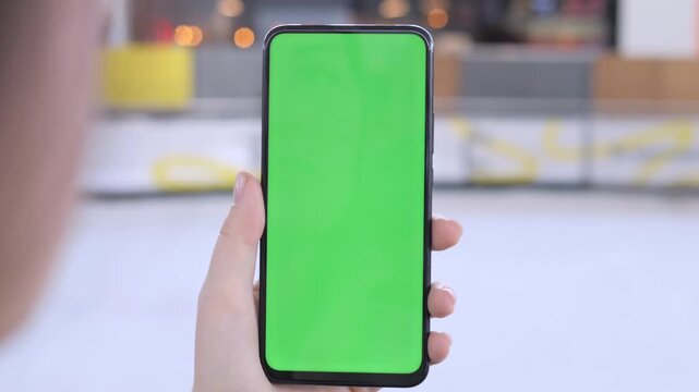 Hand holds phone with green screen. Focus on screen, blurred background. Person appears calm and focused. Ideal for app or advertisement mockups. Perfect for digital marketing or tech presentations