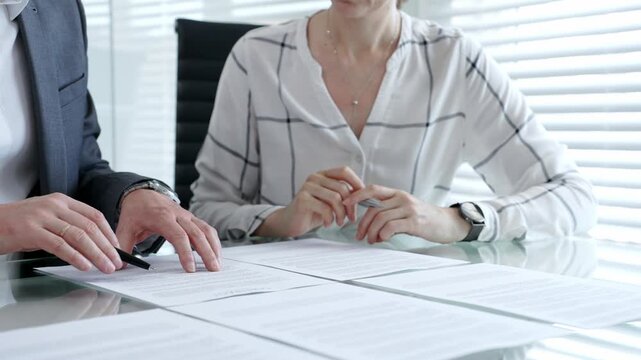 Business professionals discussing a contract, agreement, or important partnership documents during a meeting in an office setting, signing paperwork for a deal