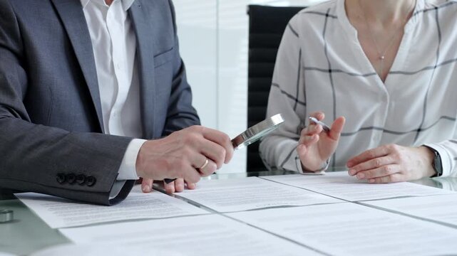 Business professionals reviewing legal contracts and important documents with a magnifying glass, performing careful examination and due diligence for risk assessment