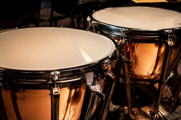 Fototapeta premium A pair of polished copper kettledrums with taut drumheads gleaming under focused stage lighting.