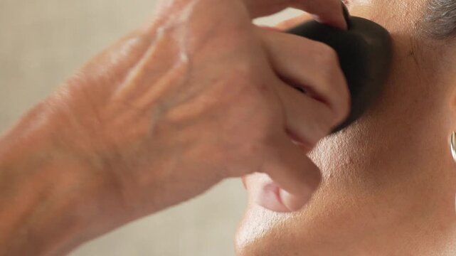 Woman applying makeup with a black beauty blender on her cheek and jawline as part of her beauty routine