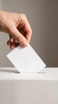 Bare hand releasing a blank paper ballot into a white ballot box slot