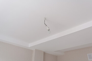 clean white ceiling features recessed cornice and a hanging bare bulb on short wire. below, beige textured walls meet at a corner, with small wall vent visible on right © evgeniykleymenov