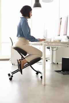 Employee working at computer in office seated on ergonomic kneeling chair with upright posture, showing healthy and correct position. Long-term comfort during desk tasks, healthy workstation setup