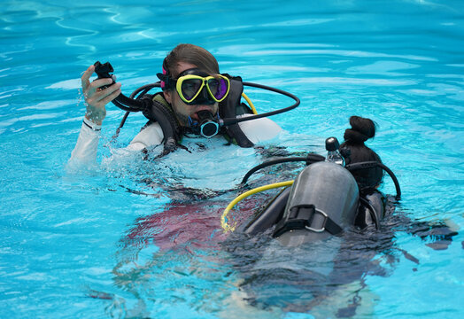 A professional diver and a novice practice diving in a pool.