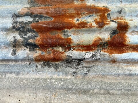 Rusted corrugated metal sheet texture with orange oxidation and weathered zinc surface