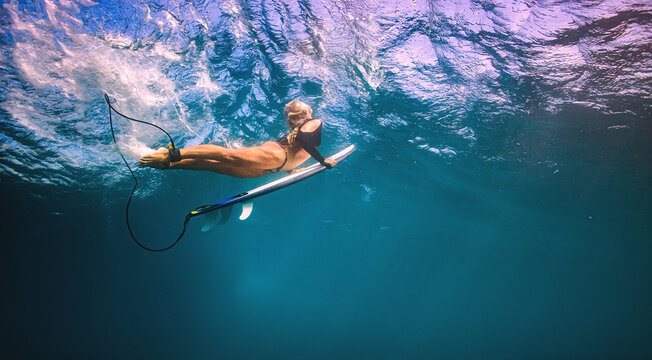 Underwater view of blonde surfer holding her white surfboard whi