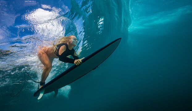 Underwater Shot of Female Surfer Paddling Beneath Massive Ocean