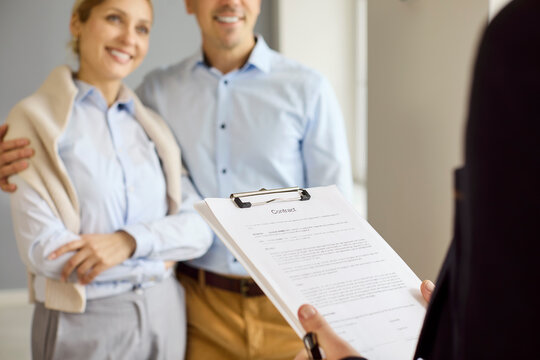 Couple realtor agent client contract signing property meeting. Smiling clients review agreement on clipboard during apartment showing, discussing purchase terms with agent. All set to sign now.