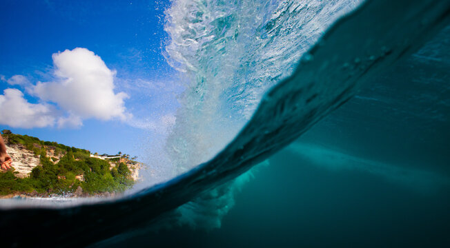 Dynamic Blue Ocean Wave Curling Over Clear Sky with Green Cliffs