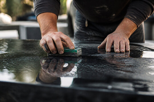 A person is polishing a dark, reflective surface with a green pad outdoors.