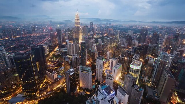 Asia, Malaysia, day to night transition time lapse of the Kuala Lumpur skyline and financial district at dusk, showing skyscrapers and the Petronas towers, high angle view 
