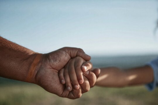 Adult hand gently holding a childs hand in a protective clasp against a soft hazy blue horizon for family lifestyle and insurance branding