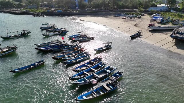 Top-down aerial footage of traditional blue wooden fishing boats neatly moored side-by-side along ropes in shallow.