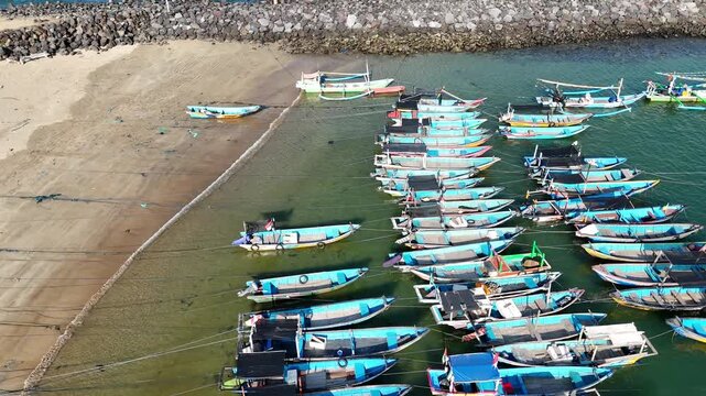 Top-down aerial footage of traditional blue wooden fishing boats neatly moored side-by-side along ropes in shallow.