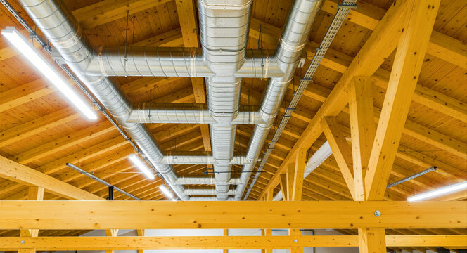 Ventilation pipes on a wooden ceiling. Modern HVAC system with timber beams and LED lighting. Engineering concept for sustainable building design.