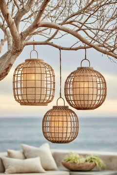 Closeup of woven rattan sphere lanterns hanging from a tree branch with a blurred ocean background and soft natural lighting creating a serene outdoor atmosphere