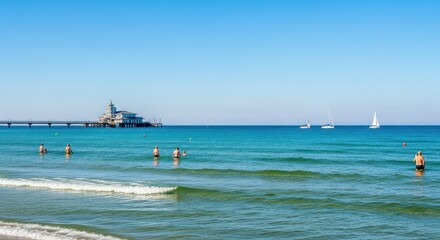 Obraz premium Bright beach scene with swimmers and distant pier.