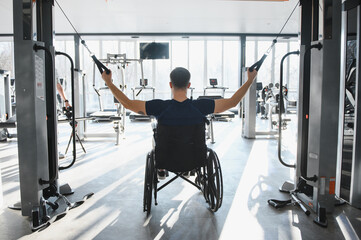 Fototapeta premium Man in wheelchair exercising arms with cable machine in gym