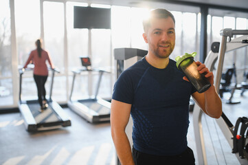 Fototapeta premium Man drinking supplement in gym after workout with treadmills in background