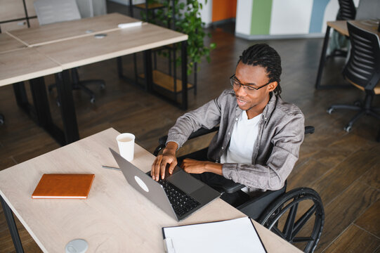 Smiling freelancer working on laptop in wheelchair at office desk