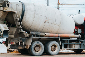 Naklejka premium A concrete mixer truck is parked at a construction site with construction equipment visible nearby. The scene shows preparation for a building project with materials and machinery scattered around