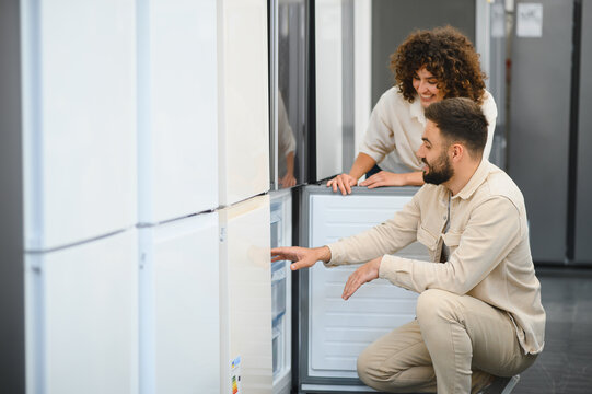 Couple choosing refrigerator in electronics store examining home appliances