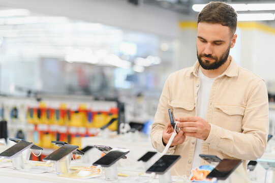 Customer choosing smartphone in electronics store, examining new mobile phone