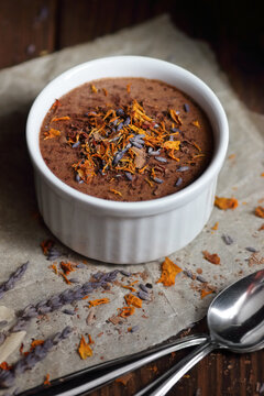 Healthy raw vegan chocolate souffle in white ramekin made of aquafaba decorated with lavender flowers and dry orange petals on dark moody background with copy space
