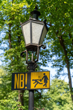 Warning sign with a pictogram alerting visitors to the risk of pickpocketing, mounted below a decorative street lantern in a public area.