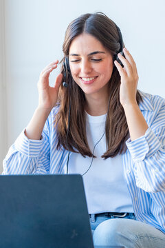 Smiling young woman wearing a headset works on a laptop during a video call, representing remote work, customer service, online meeting and friendly virtual communication in a bright home office 